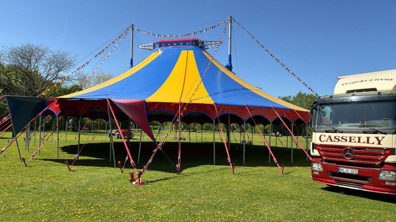 Das blau-gelbe Circuszelt mit Wimpelketten und dem Casselly-Truck auf der Wiese