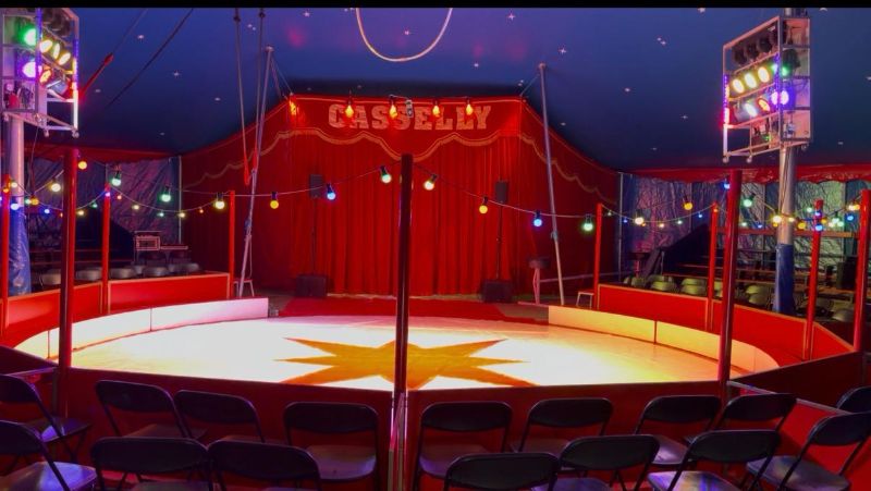 Die Manege im Circuszelt mit rotem Vorhang, bunten Lichterketten und Sternenhimmel